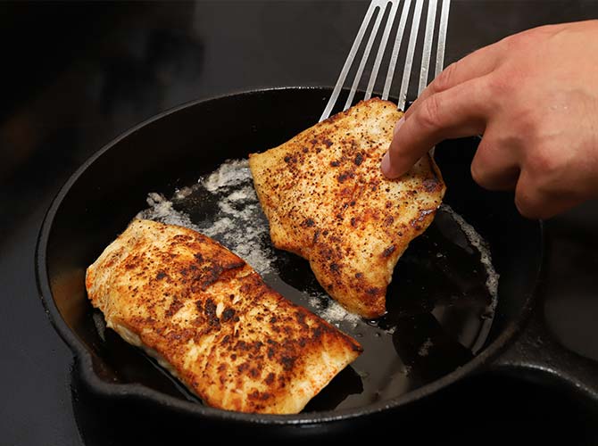 Flipping two pieces of halibut in a cast iron pan